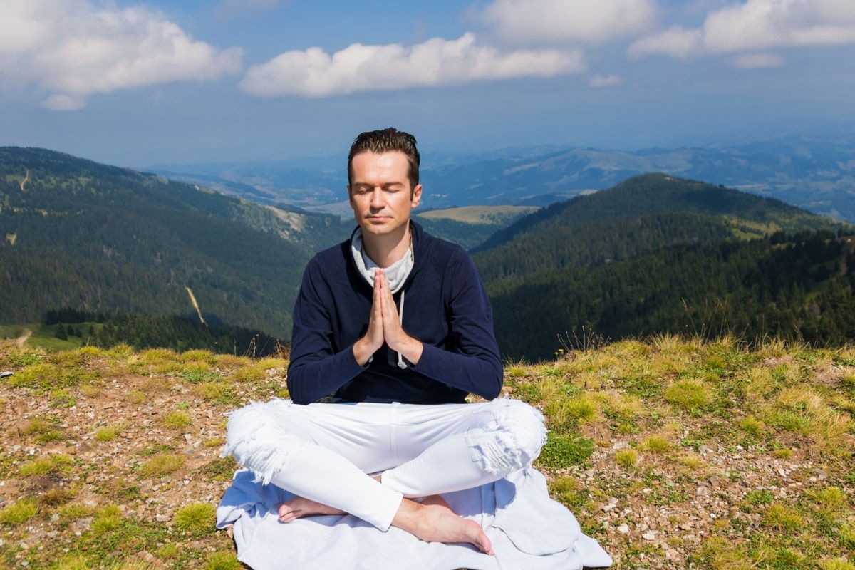 Peaceful man meditating in namaste pose on top of the mountain. Practicing Yoga and breathing fresh air on mountain peak.