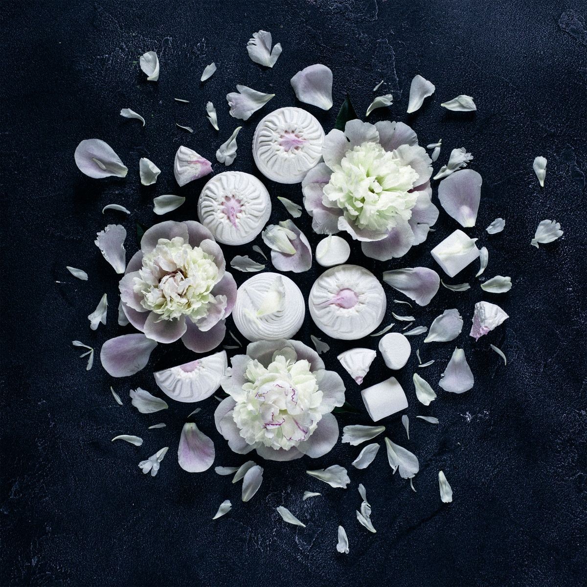 White marshmallow of different shapes and white flowers on a dark background in the form of a square
